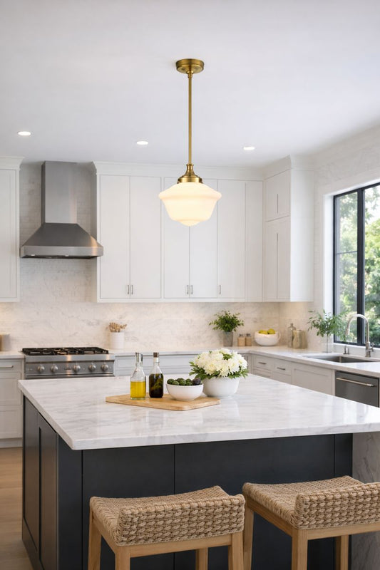 Gold schoolhouse pendant light in modern kitchen with white glass shade and brass finish, illuminating marble island.